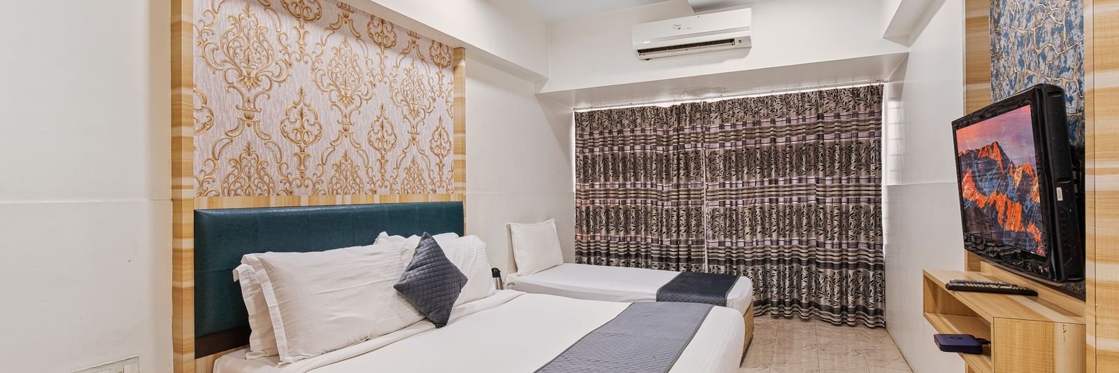 Modern hotel room with a king size bed and a singe bed at Mayur Retreat, contemporary lighting, and a flat-screen TV for a comfortable stay.