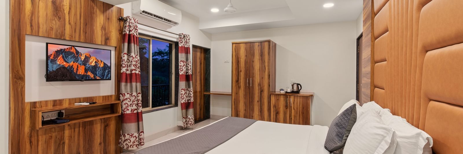 Comfortable guest room at Mayur Retreat with a white bed, cushioned headboard, and wall-mounted TV.