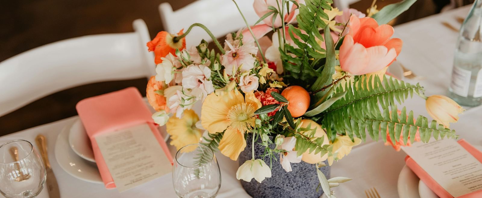 A vibrant floral centrepiece featuring an assortment of flowers, sits on a table set for an event.