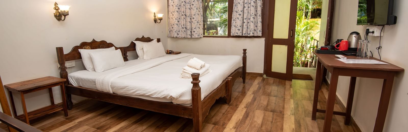 Bright guest room with a double bed, wooden flooring, a flat-screen TV, and natural light streaming in at De Soul Santé, Morjim.