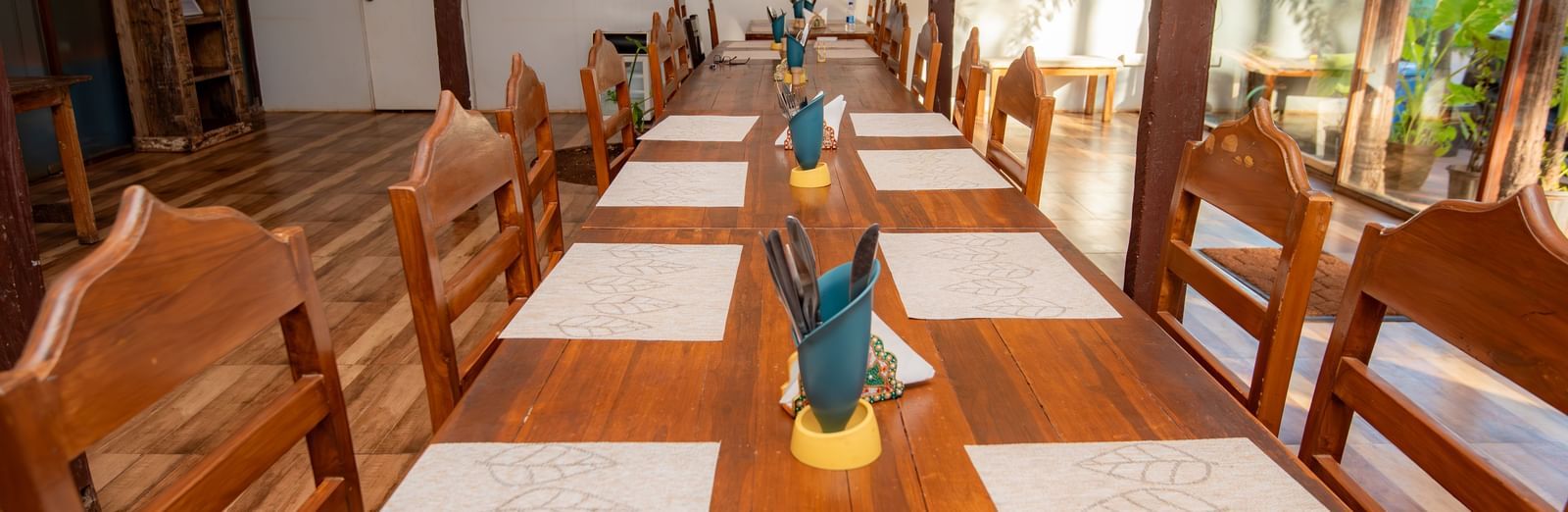 Dining table set for guests with colourful decor and wooden chairs at De Soul Santé, Morjim.
