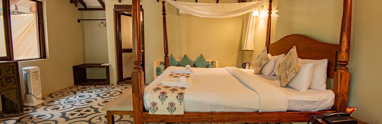 Side view of the spacious room with a large bed, bedside wooden table, and wooden-panelled ceiling at De Soul Santé, Morjim.