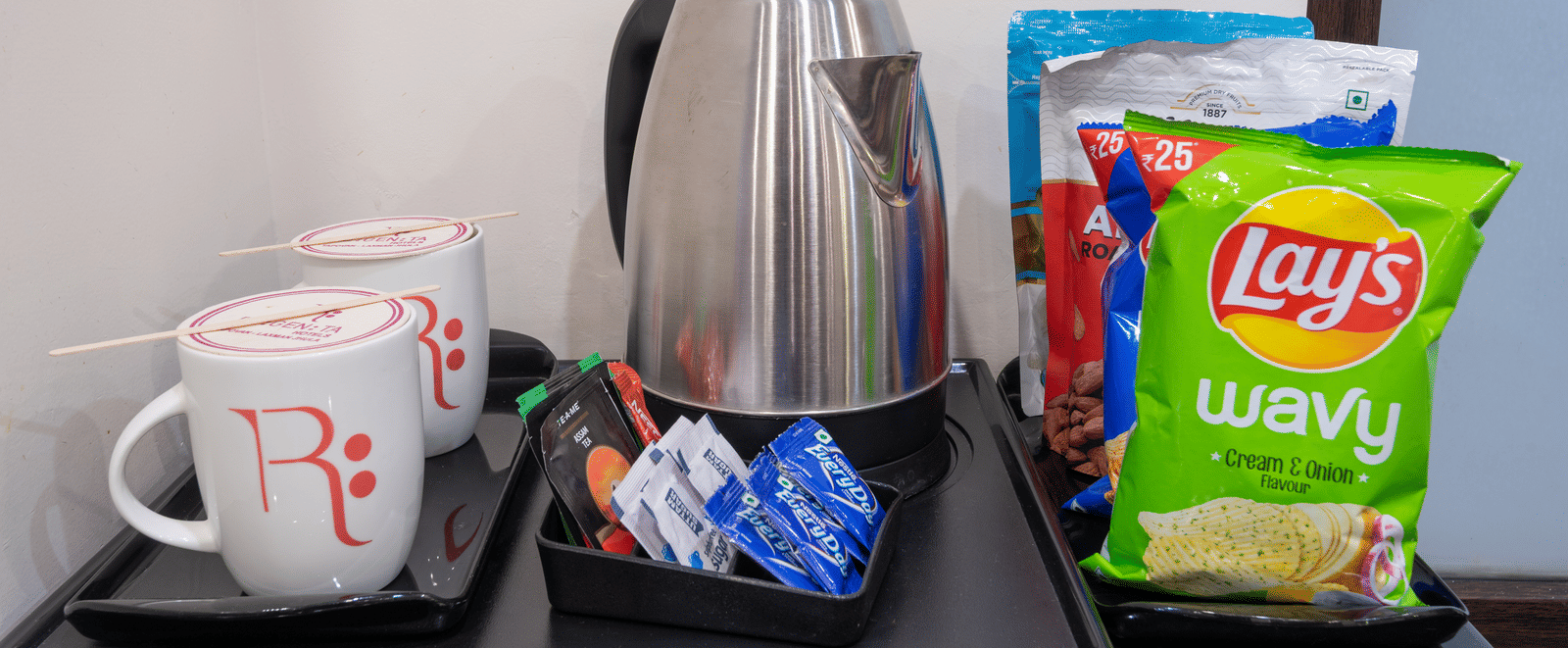 Tea and coffee maker with kettle, mugs, and snacks at DLS Hotels On The Ganges.