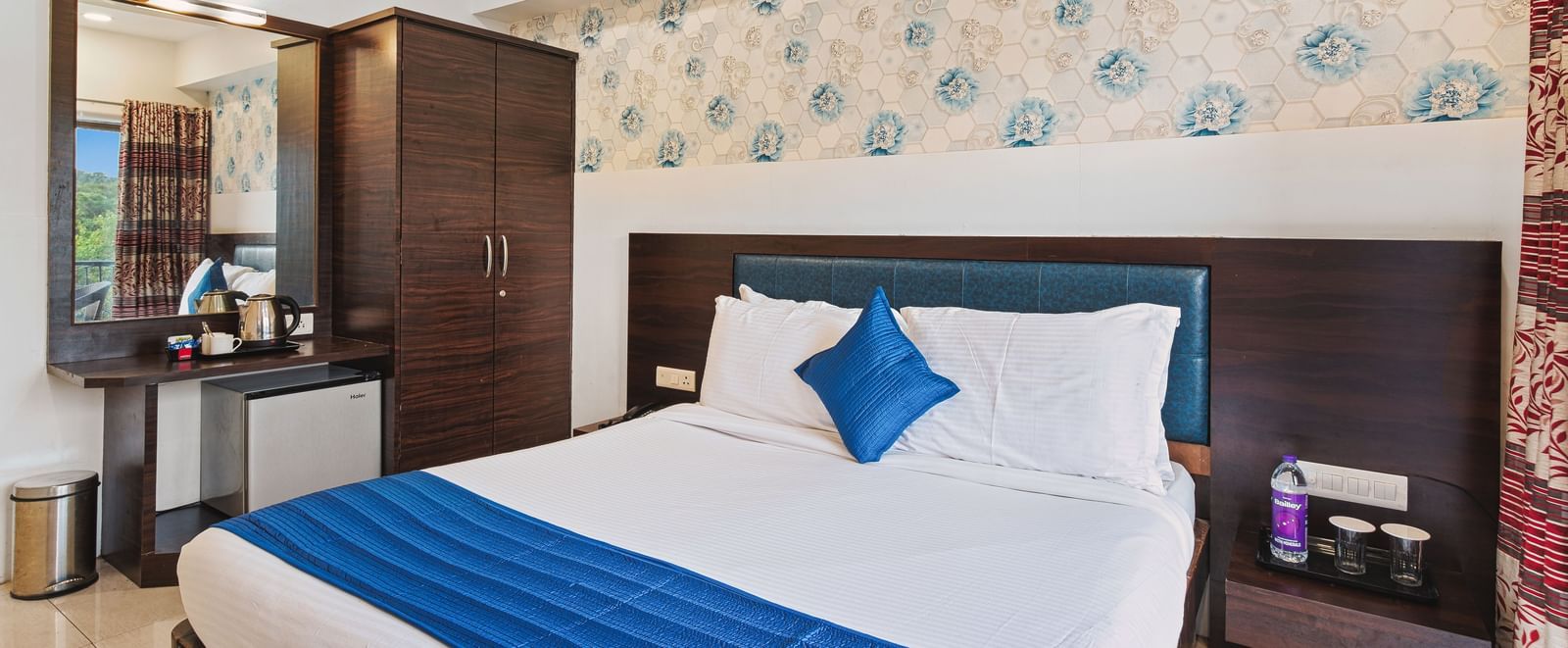 Contemporary bedroom at Mayur Retreat with blue-accented bed, floral wallpaper, and ambient lighting.