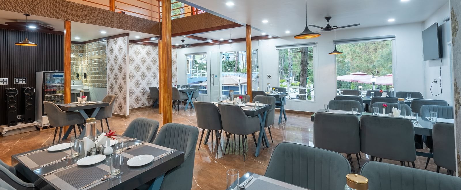 Contemporary restaurant dining area with neatly set tables, cushioned chairs, ceiling fans, and large windows providing natural light - DLS Nature Trinket Resort, Dalhousie.