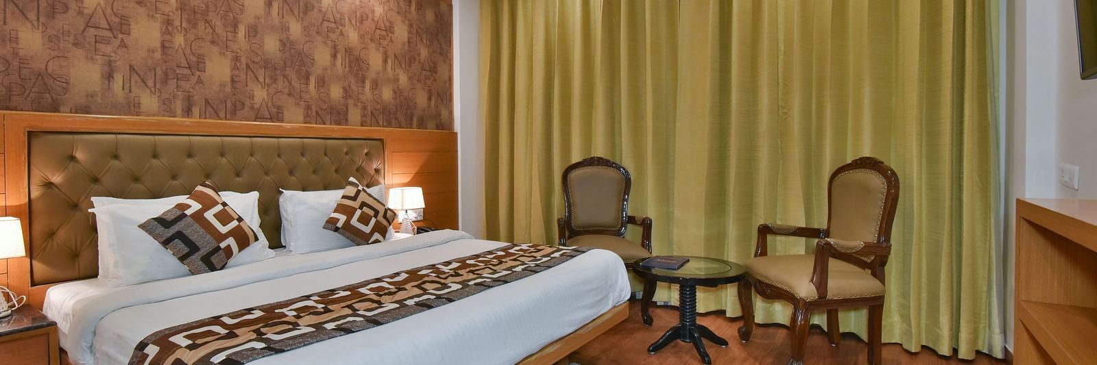 A large bed placed next to two chairs in the Deluxe Room at DLS Highland Resort and Spa, Mussoorie.