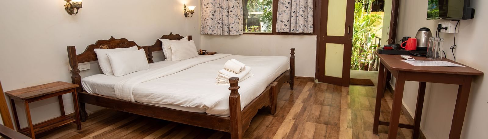 Bright guest room with a double bed, wooden flooring, a flat-screen TV, and natural light streaming in at De Soul Santé, Morjim.
