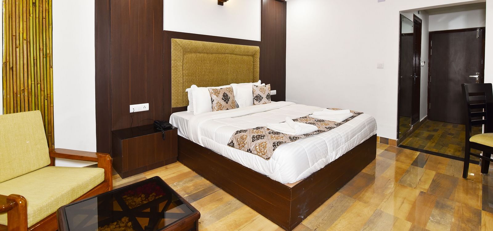 Image of a room with wooden interiors featuring a king size bed, a sofa and a table in a well lit environment | DLS Kapoor Resort Manali