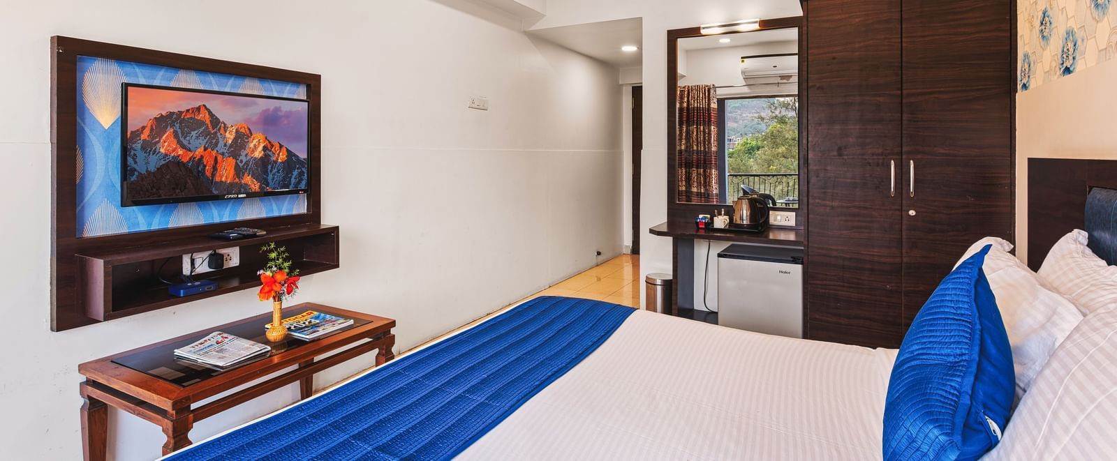 King size bed room at Mayur Retreat with a blue-accented bed, flat-screen TV, and wooden furniture.