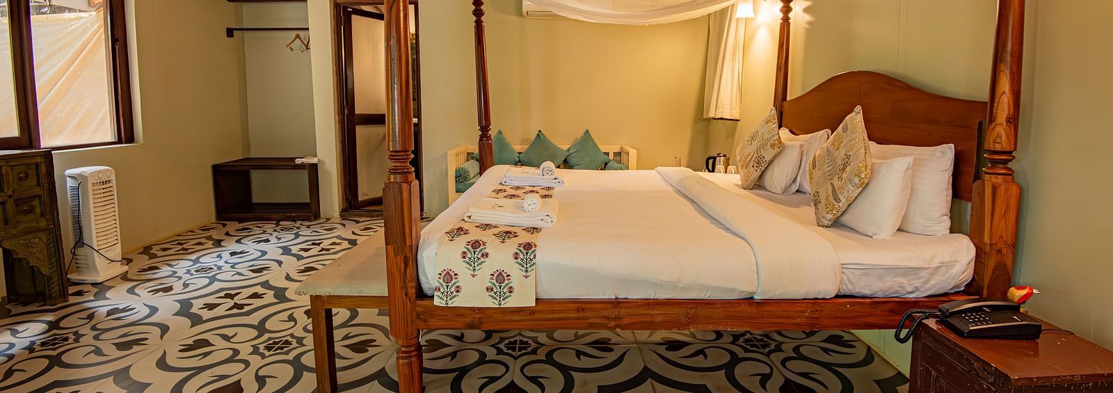 Side view of the spacious room with a large bed, bedside wooden table, and wooden-panelled ceiling at De Soul Santé, Morjim.