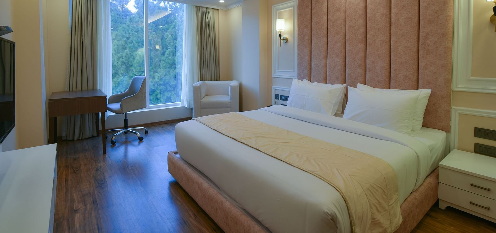 A bright and spacious hotel room with a king-sized bed, stylish decor, and large windows offering stunning views of the surrounding hills.