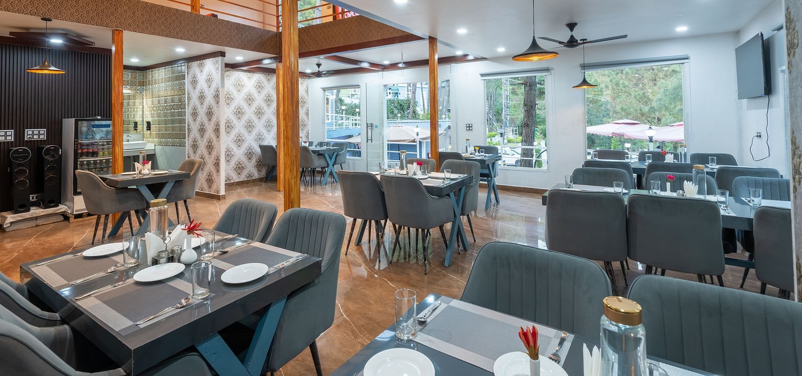 Contemporary restaurant dining area with neatly set tables, cushioned chairs, ceiling fans, and large windows providing natural light - DLS Nature Trinket Resort, Dalhousie.