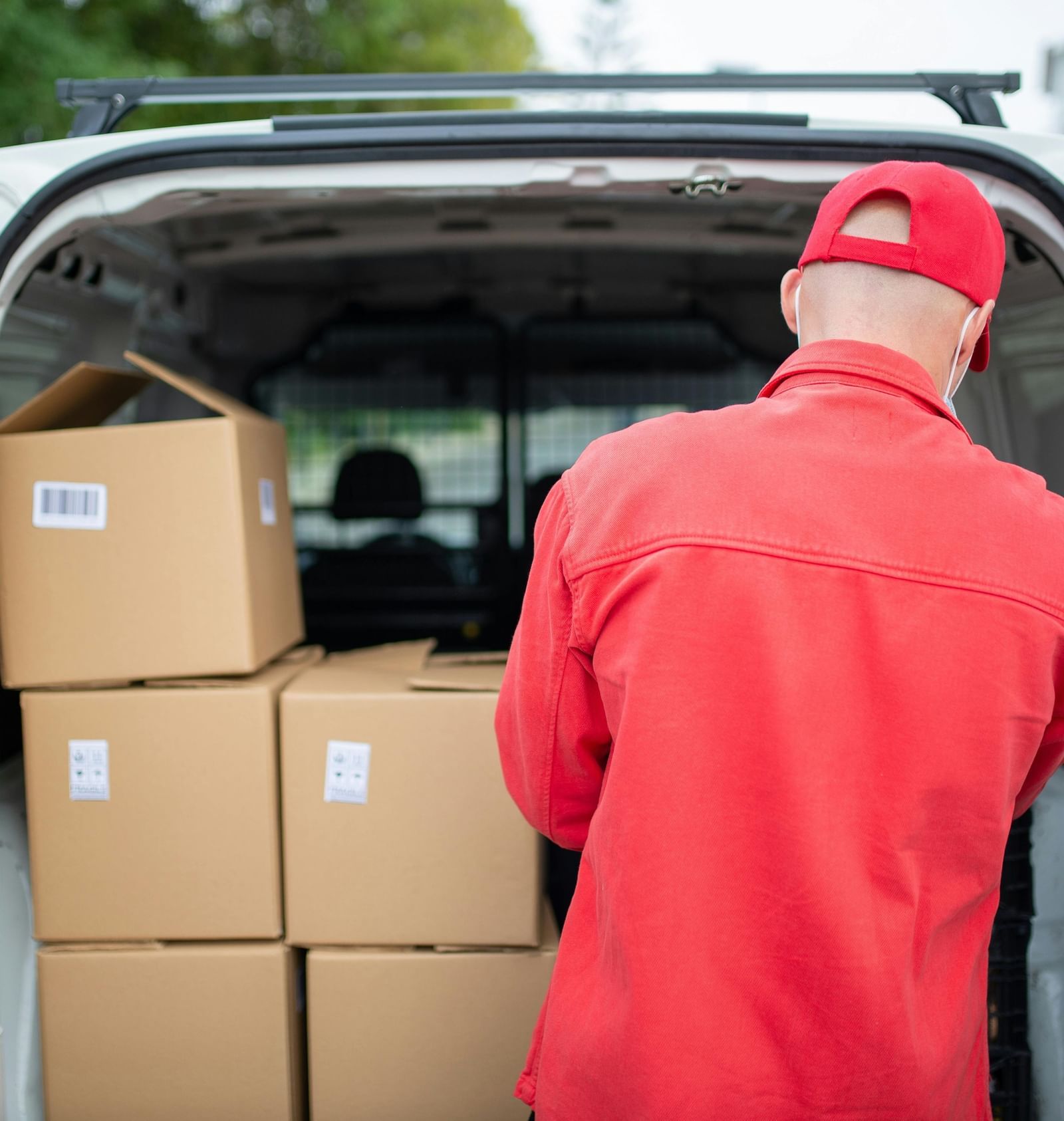 A delivery person in a red uniform loading cardboard boxes into the back of a white van.