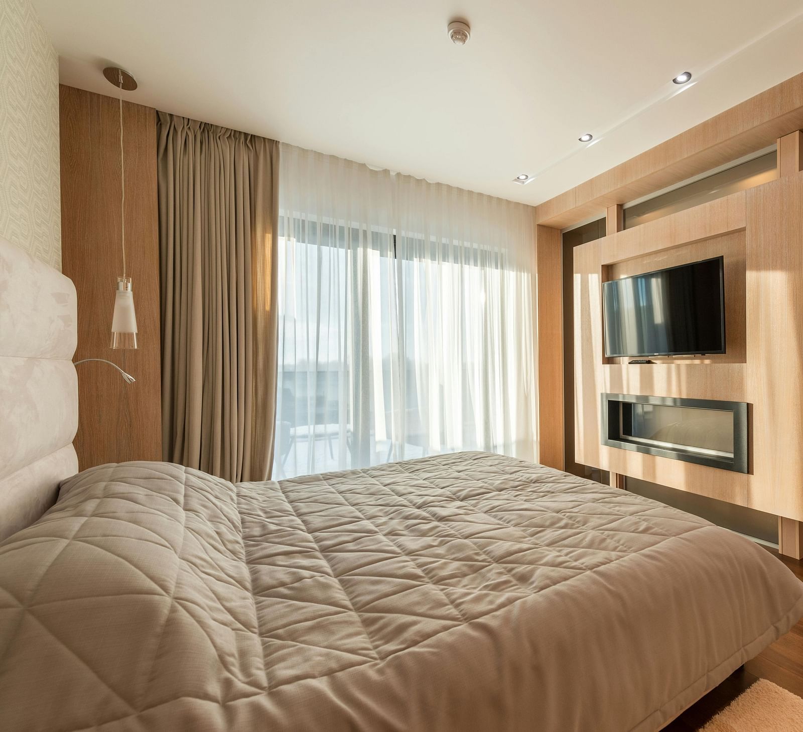 An image of a room with a king size bed, flat screen TV, decorative items, and an expansive window with curtains