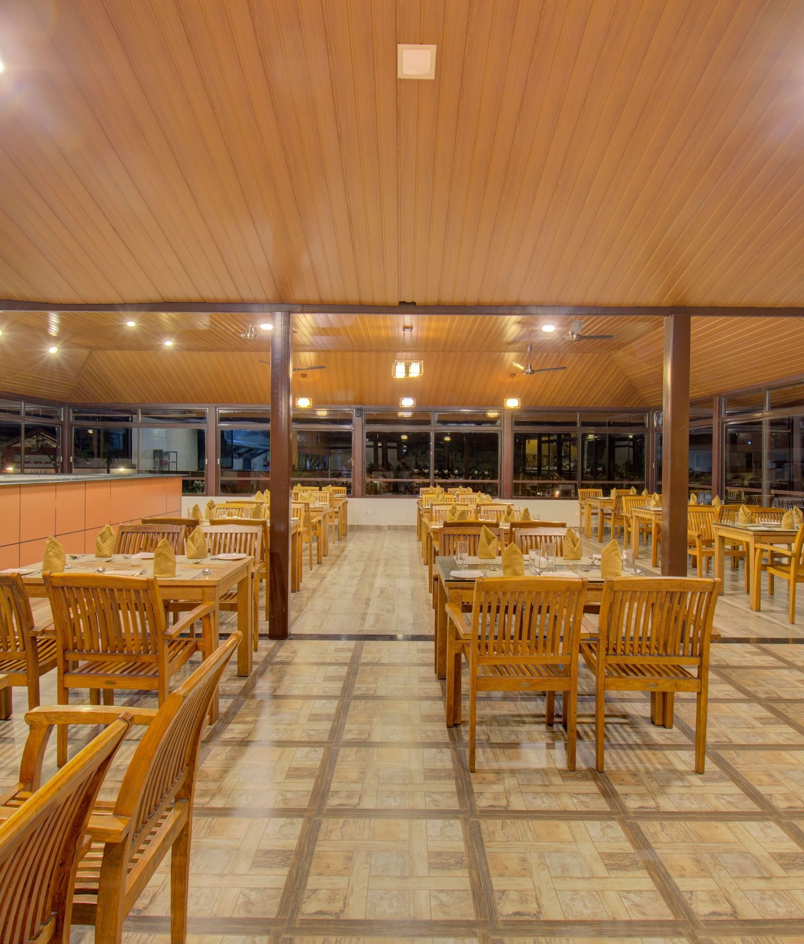 A spacious dining area with wooden tables and chairs, illuminated by warm lighting | Sheesham Restaurant | Woodstock Resorts, Coorg