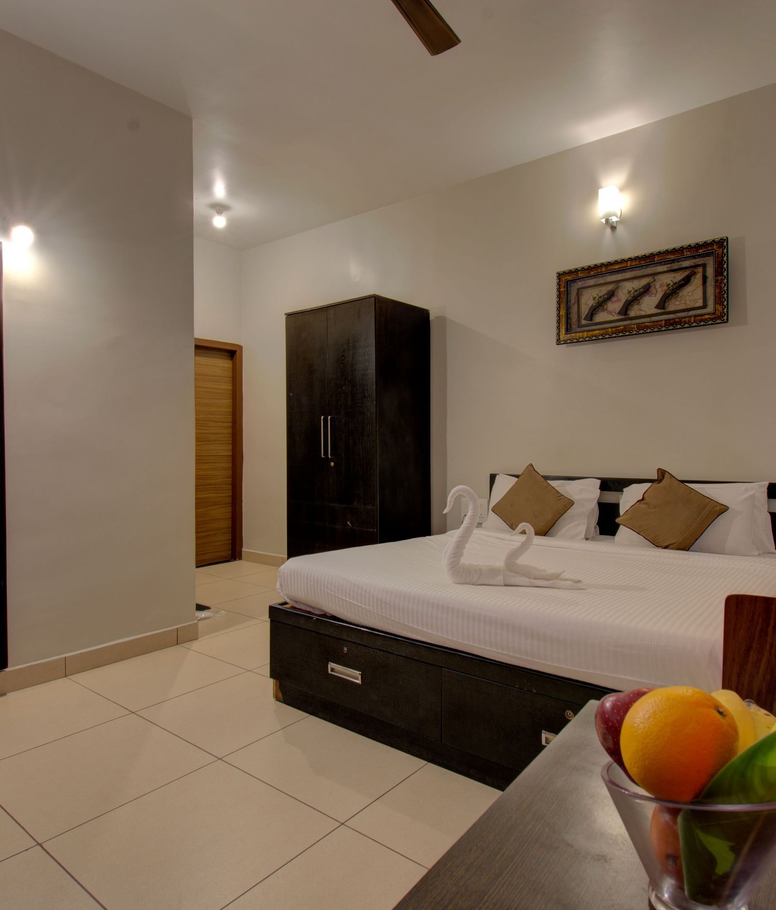 A bedroom with a huge bed, a mirror, Cupboard, a table with fruits on it | Superior Room | Woodstock Resorts, coorg