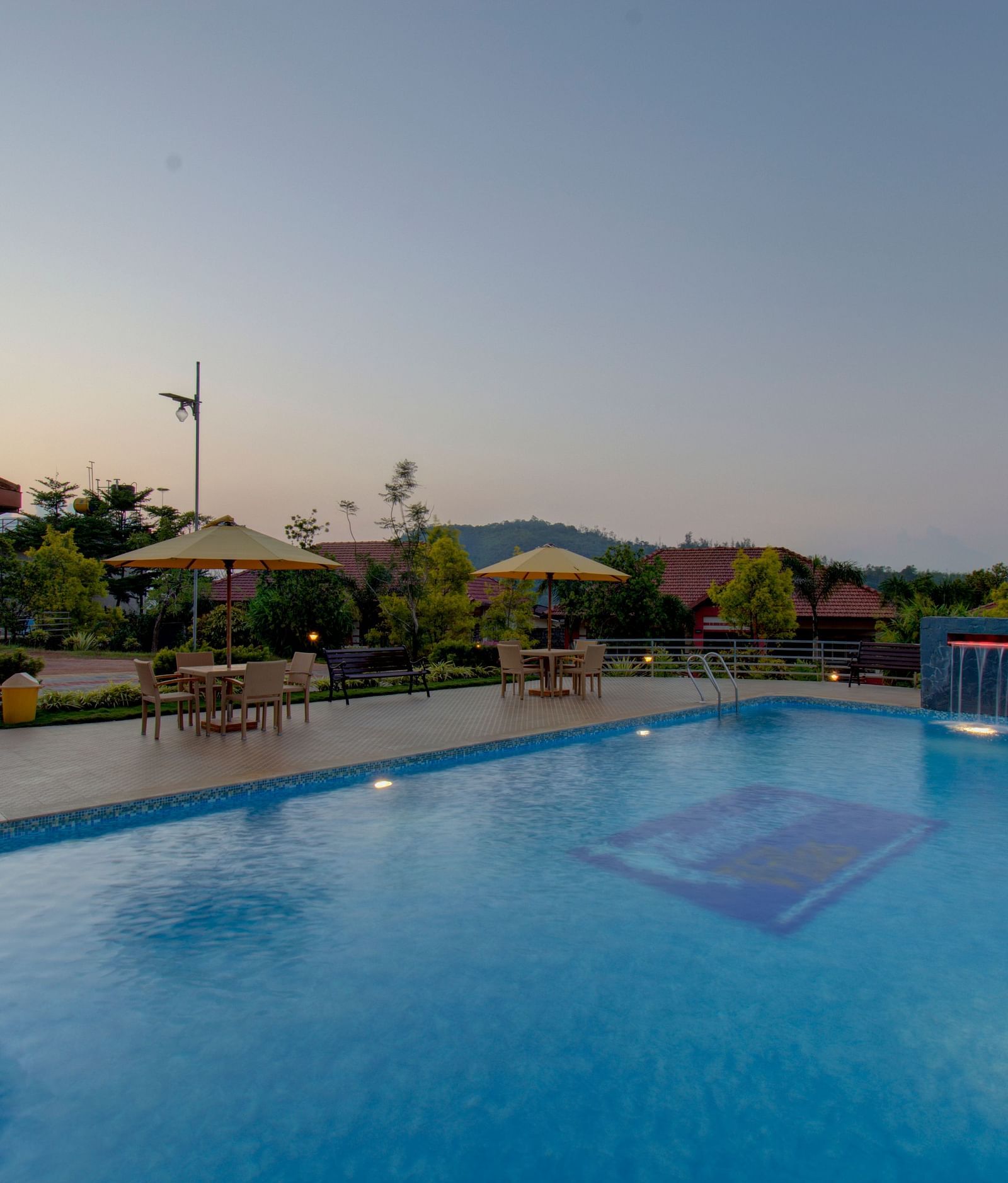 Swimming pool with patios with hills in the background | Woodstock Resorts, Coorg