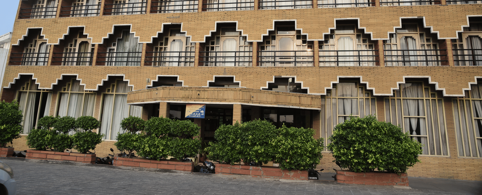 Exterior shot of Hotel Gold, Panipat taken in the morning with dense green bushes in the entrance.