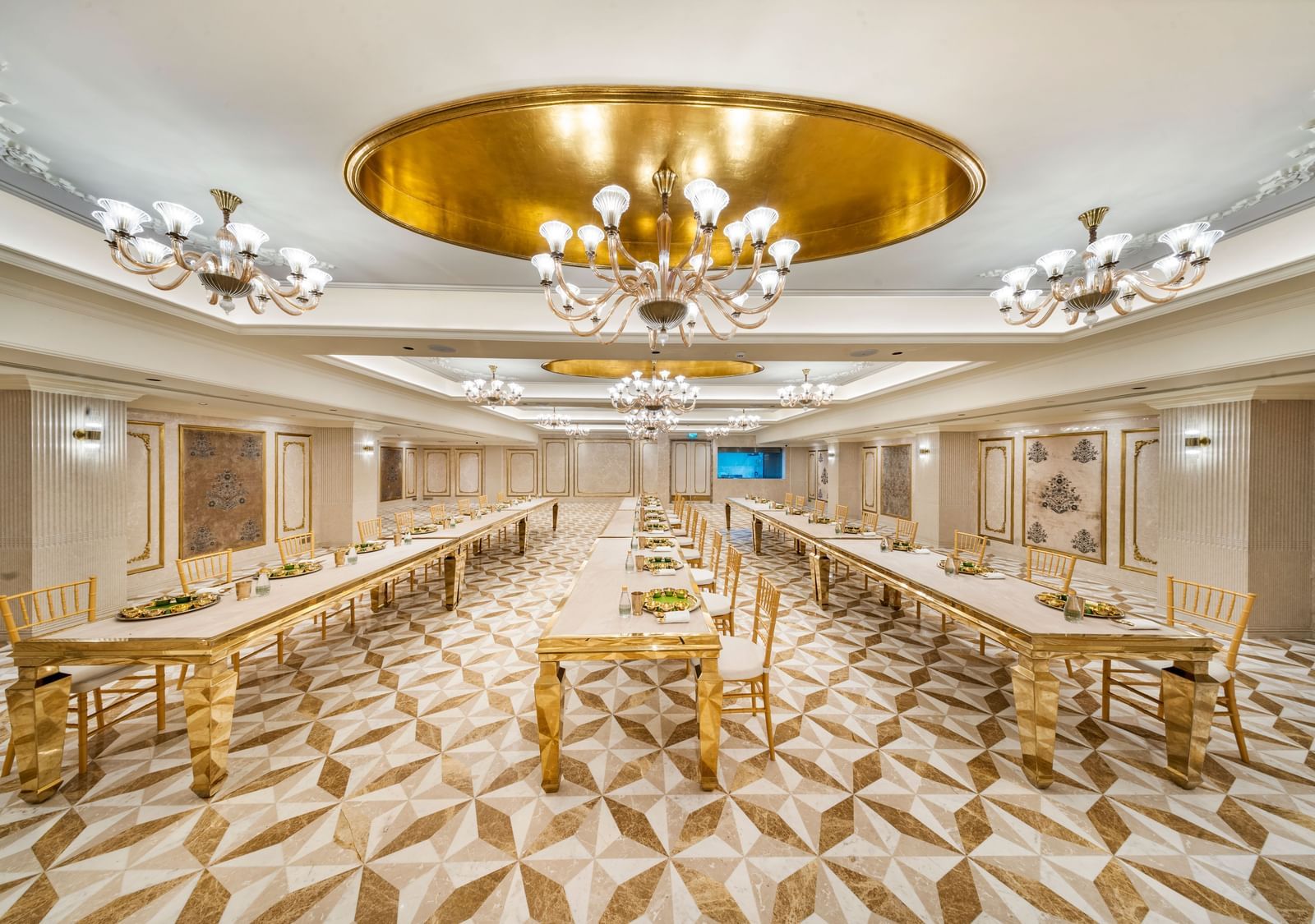 A lavish banquet hall at Grand Chennai by GRT Hotels, showcasing numerous golden tables and chairs under exquisite chandeliers.