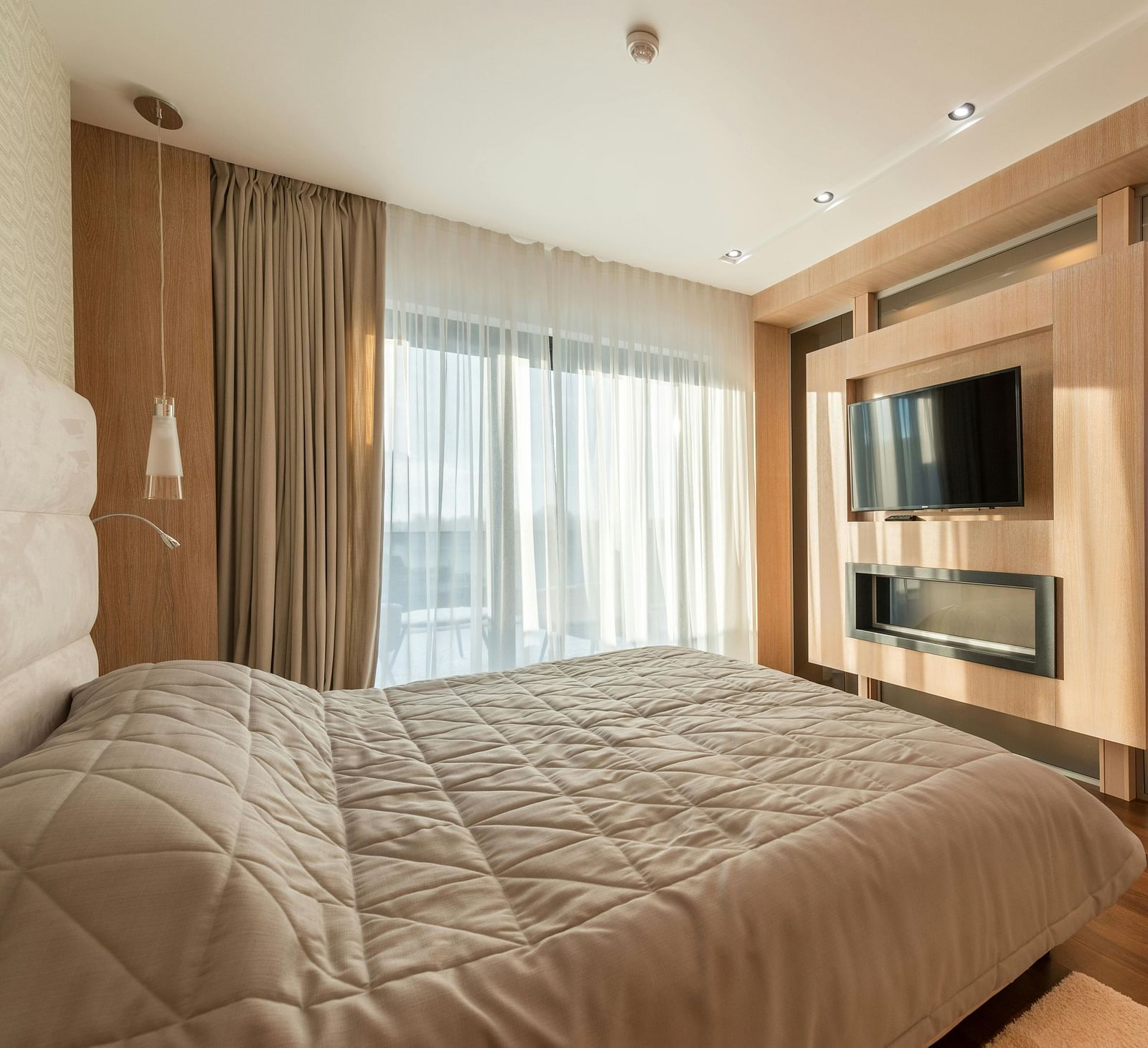 An image of a room with a king size bed, flat screen TV, decorative items, and an expansive window with curtains