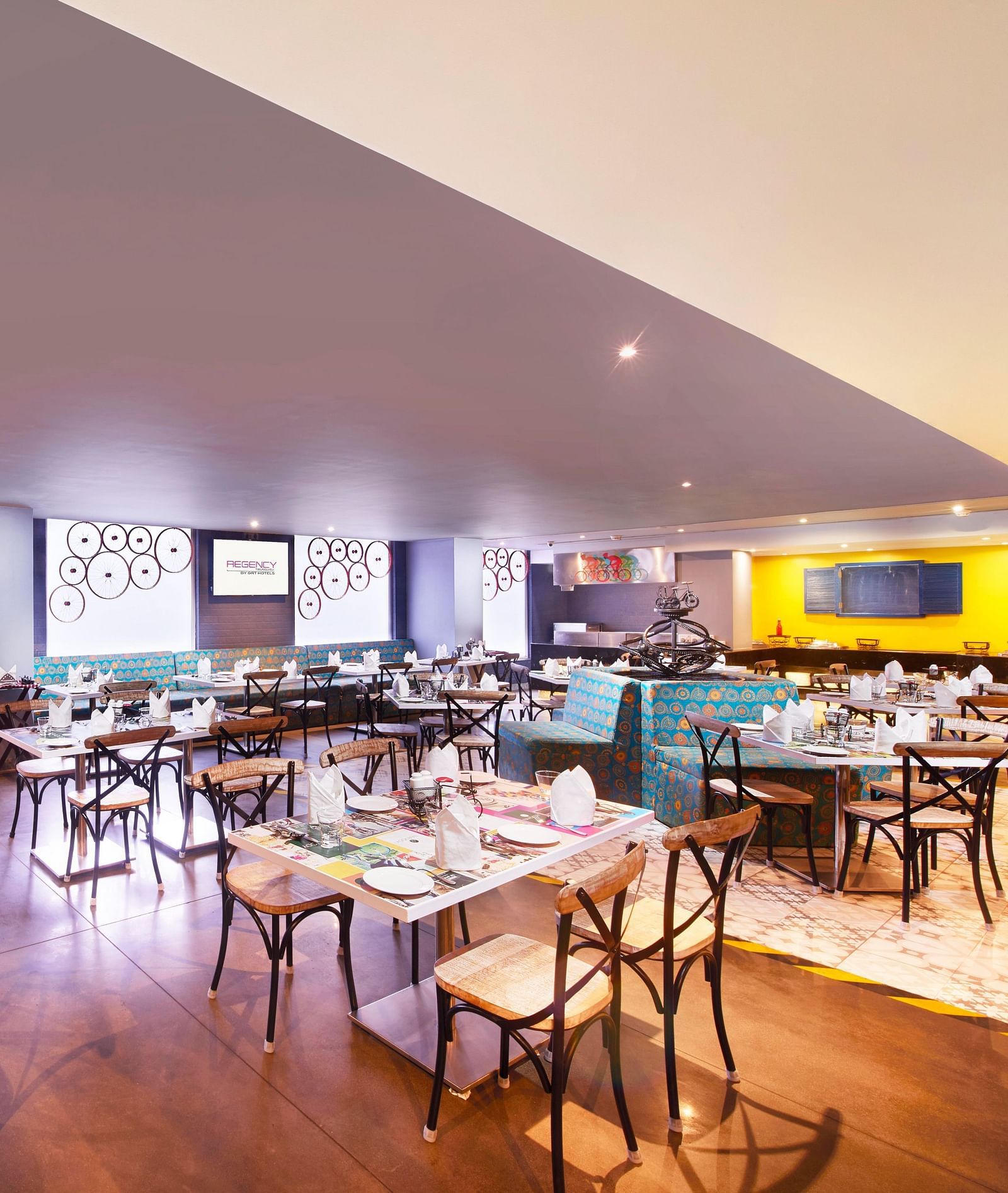 A brightly lit restaurant with chairs, a long bar counter, and a colorful wall mural | Regency Tirunelveli By GRT Hotels