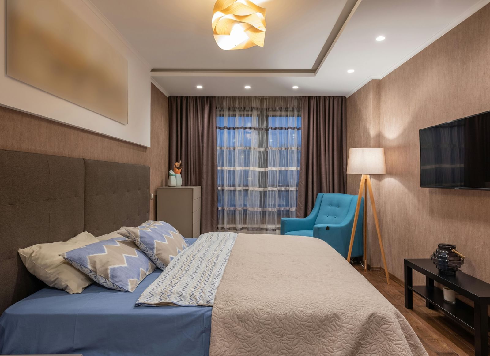 Cosy hotel room with large bed, soft lighting, modern decor, and a wall-mounted TV