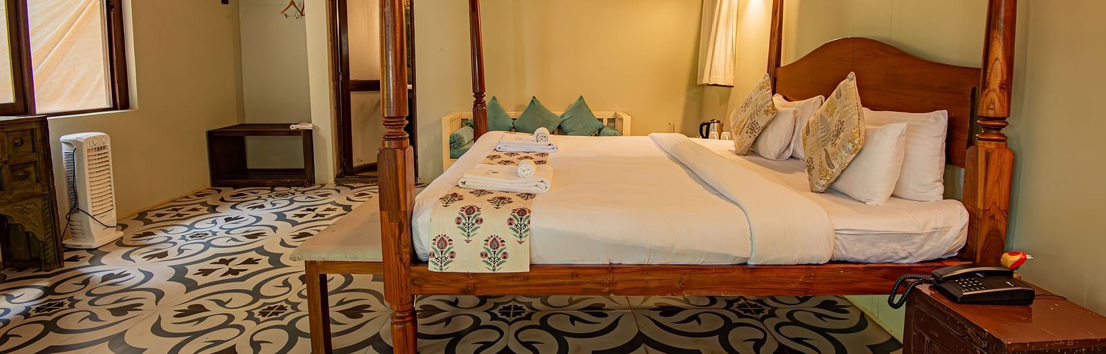 Side view of the spacious room with a large bed, bedside wooden table, and wooden-panelled ceiling at De Soul Santé, Morjim.