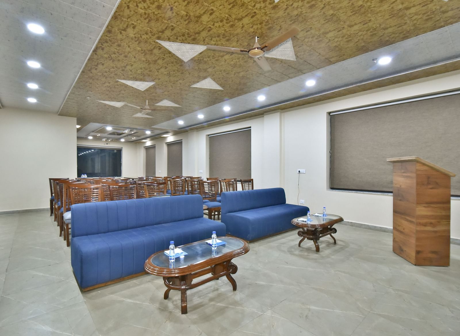 A banquet hall with a blue sofa and wooden chairs facing the podium at DLS Ark Holiday Inn, Banikhet.