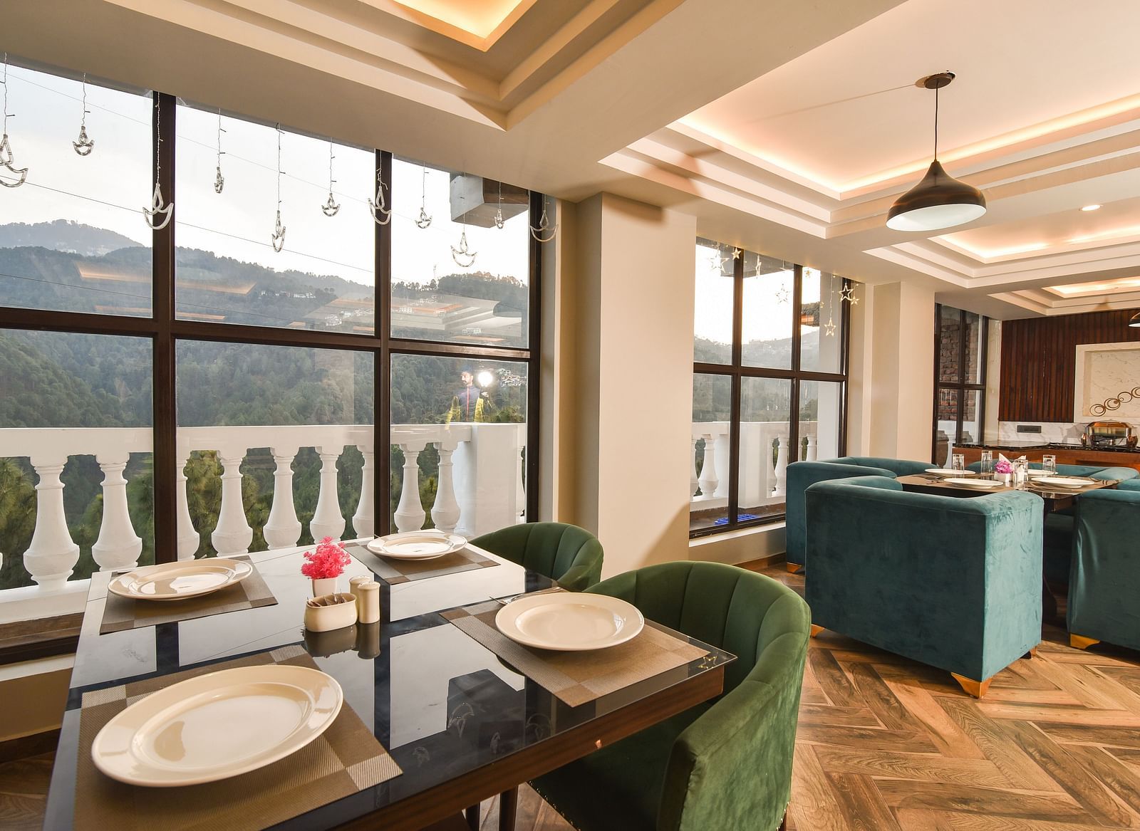 A spacious dining area with green upholstered chairs and a table set for a meal, offering panoramic views through large windows. The room is bright and elegant, with a modern design