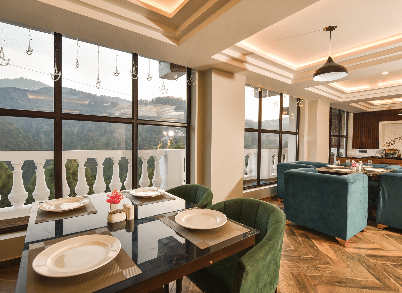A dining area with large windows offering beautiful views of the surrounding landscape. The room features green upholstered chairs and elegant decor.