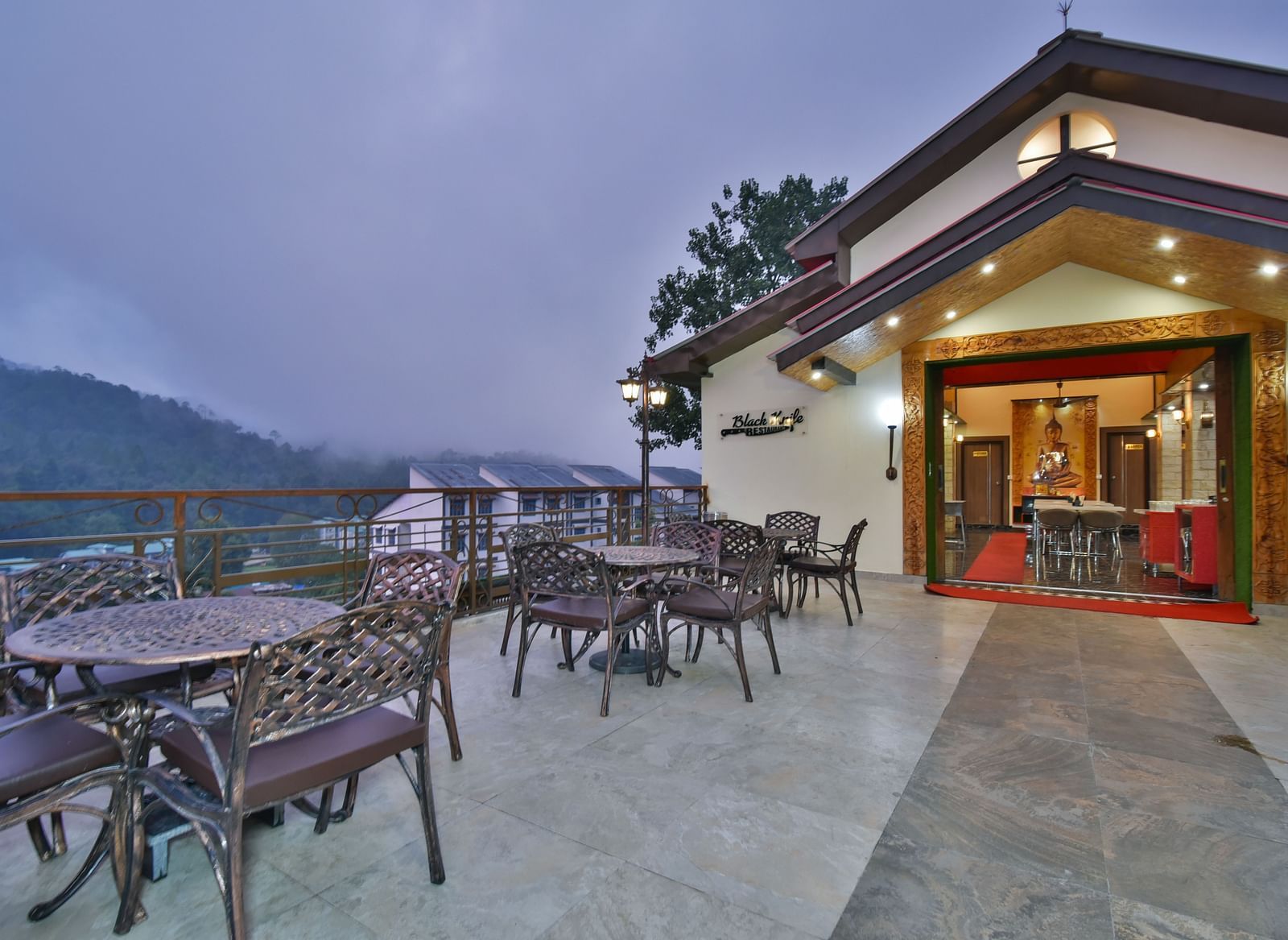 Open terrace at DLS Dalhousie Valley Resort featuring chairs and tables with backdrop of misty mountains.