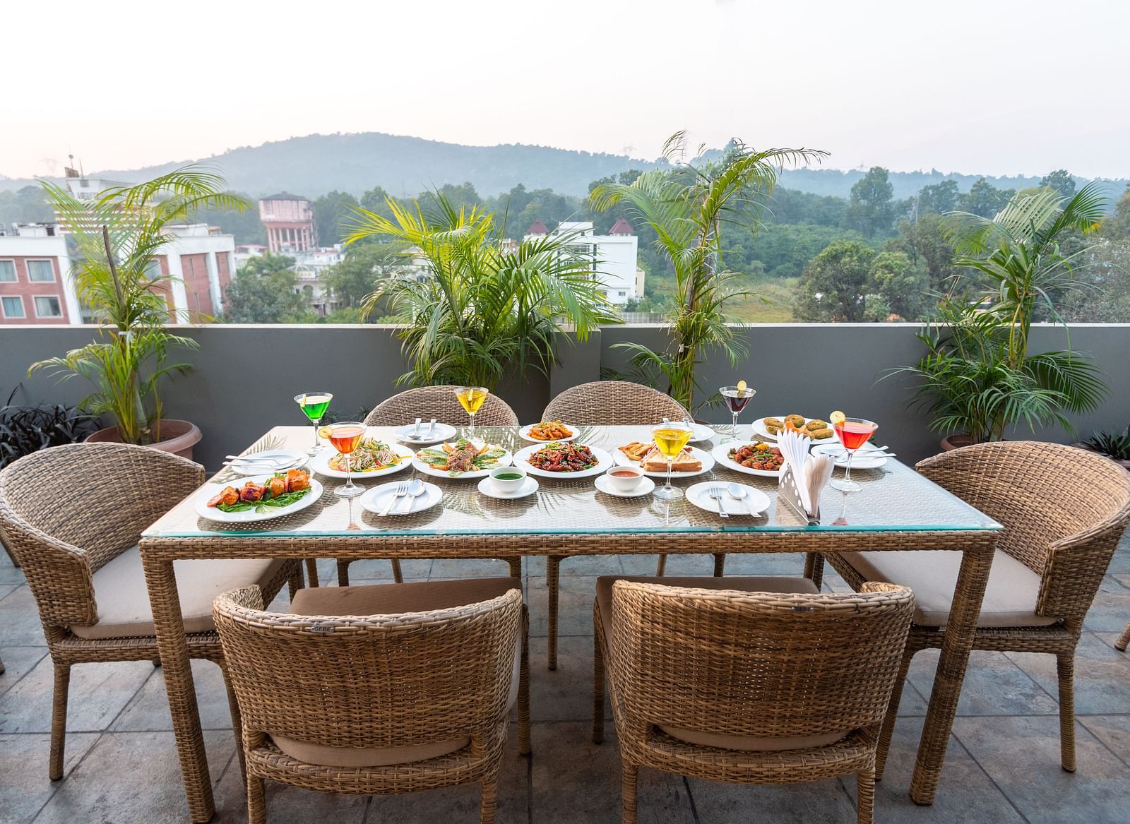 A shot of the dining area on the roof top with a table and chairs and the backdrop of the city view - DLS Hotel Arihant, Haridwar