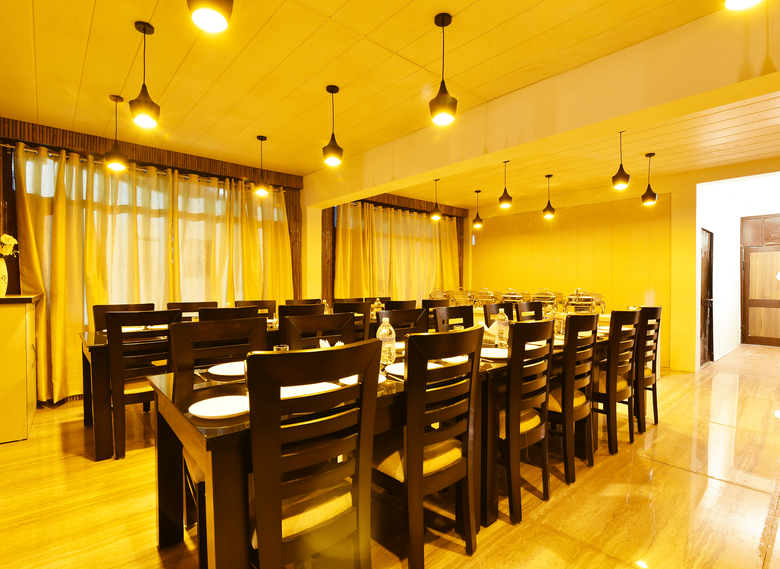 A shot of the dining table at the restaurant featuring woodden tables and chairs | DLS Kapoor Resort Manali