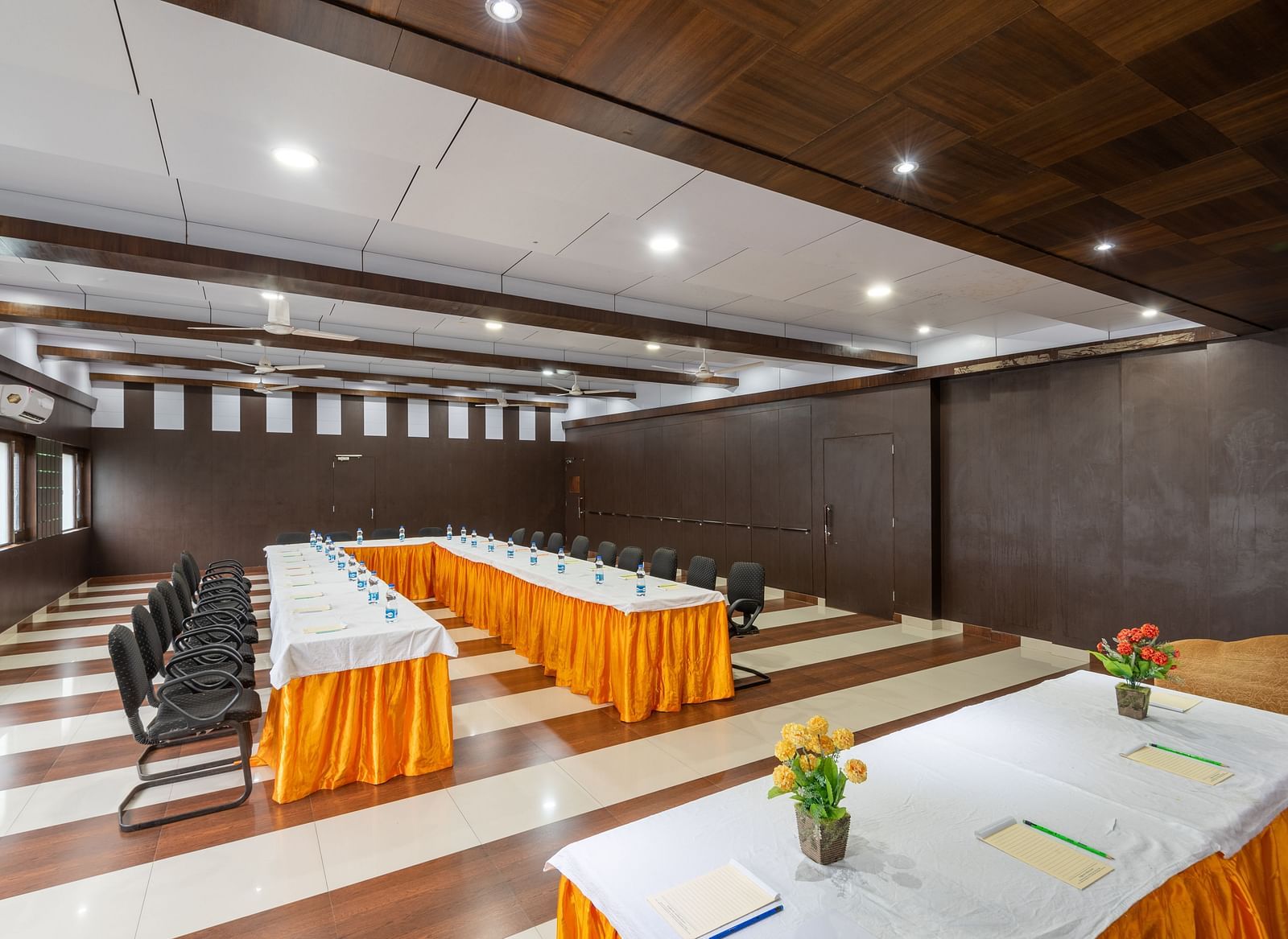 A conference room with a long table, chairs, and decorative flowers on the table. The room features wooden paneling and a checkered floor - DLS Meghavan Resort, Dharamshala