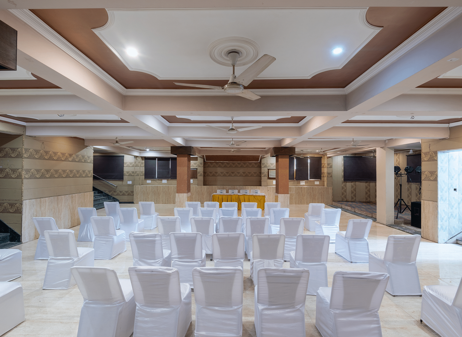 A banquet hall with chairs arranged for guests, featuring a ceiling fan, captured from the back at DLS Park Grace, Haridwar.