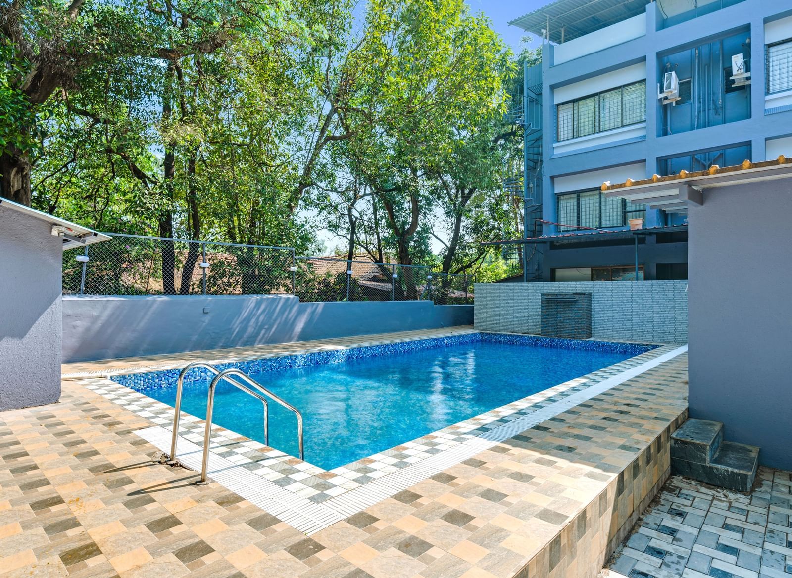 Outdoor swimming pool surrounded by trees and tiled flooring at Emerald Retreat, Tungarli.