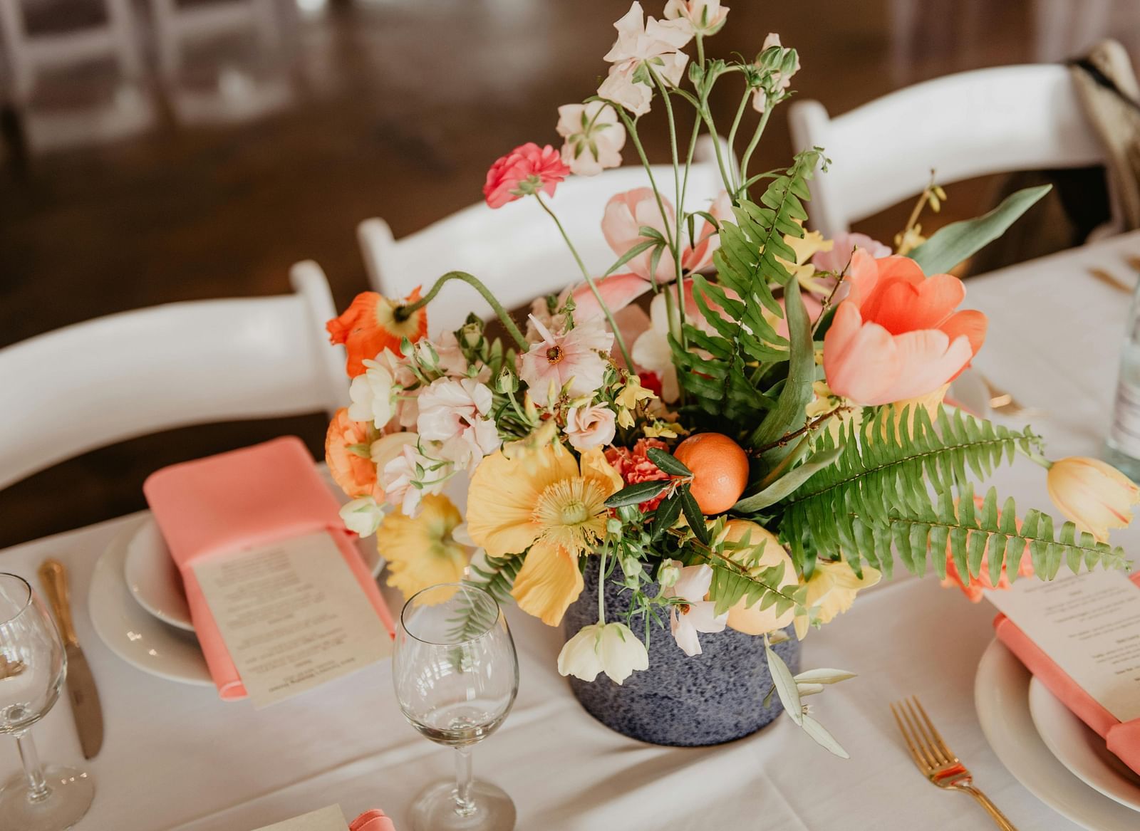 A vibrant floral centrepiece featuring an assortment of flowers, sits on a table set for an event.