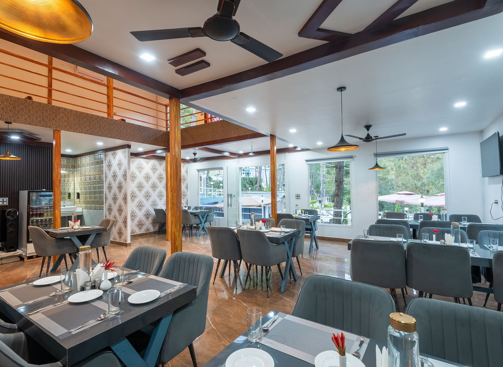 Contemporary restaurant dining area with neatly set tables, cushioned chairs, ceiling fans, and large windows providing natural light - DLS Nature Trinket Resort, Dalhousie.