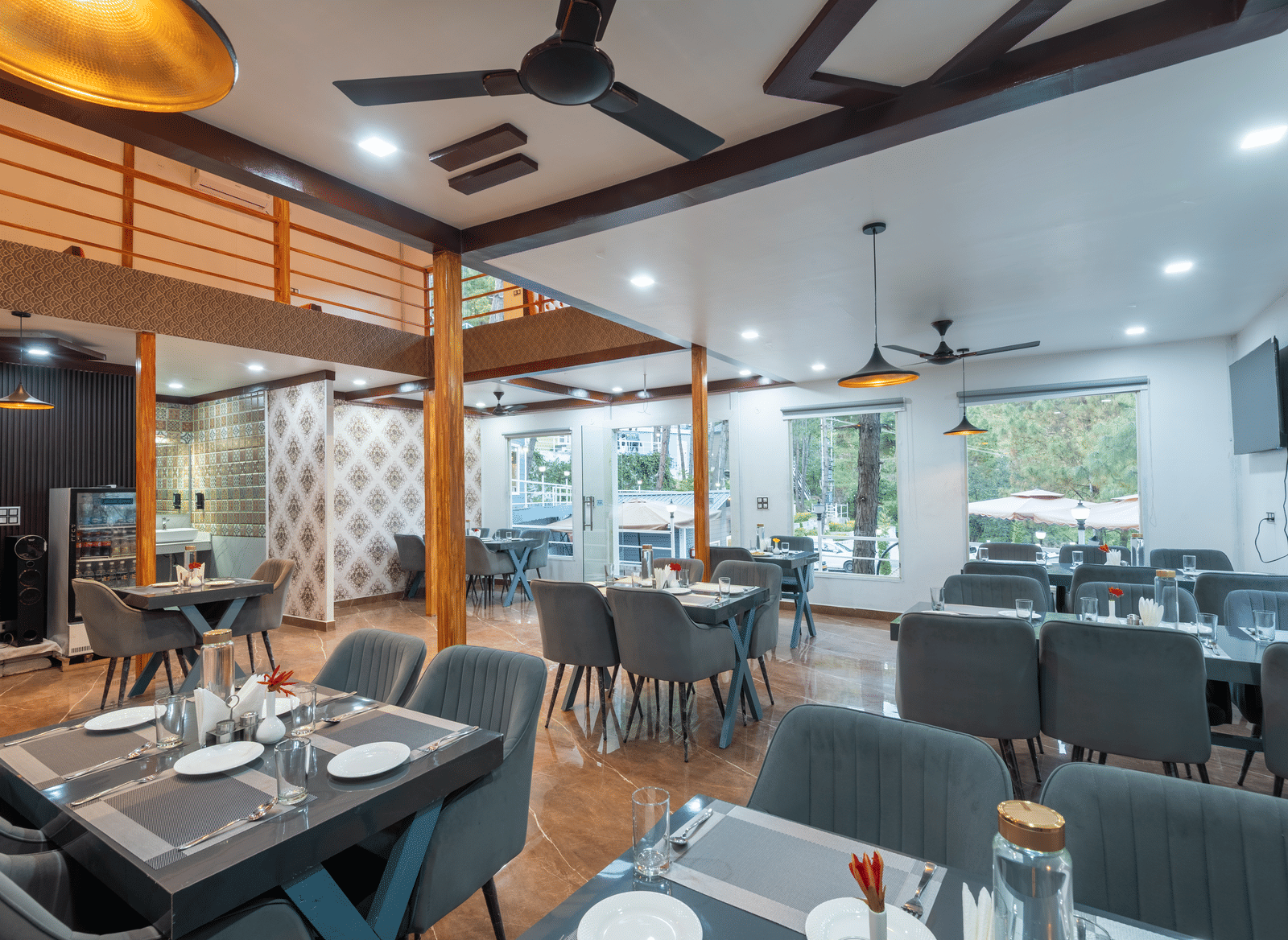 A contemporary restaurant area with neatly set tables, cushioned chairs, ceiling fans, and large windows providing natural light - DLS Nature Trinket Resort, Dalhousie