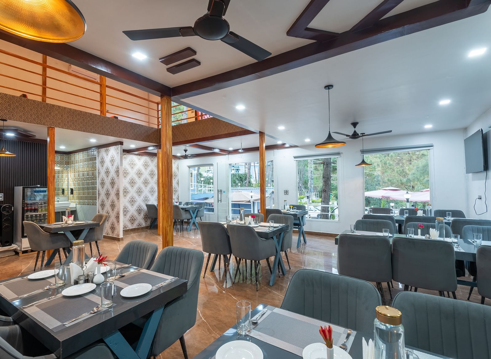 Contemporary restaurant dining area with neatly set tables, cushioned chairs, ceiling fans, and large windows providing natural light - DLS Nature Trinket Resort, Dalhousie.