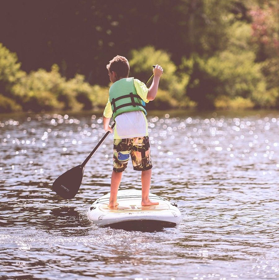 The image shows a boy paddle boarding on a lake.