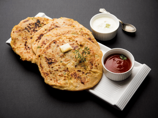 Parathas with raita, butter and ketchup served on a platter