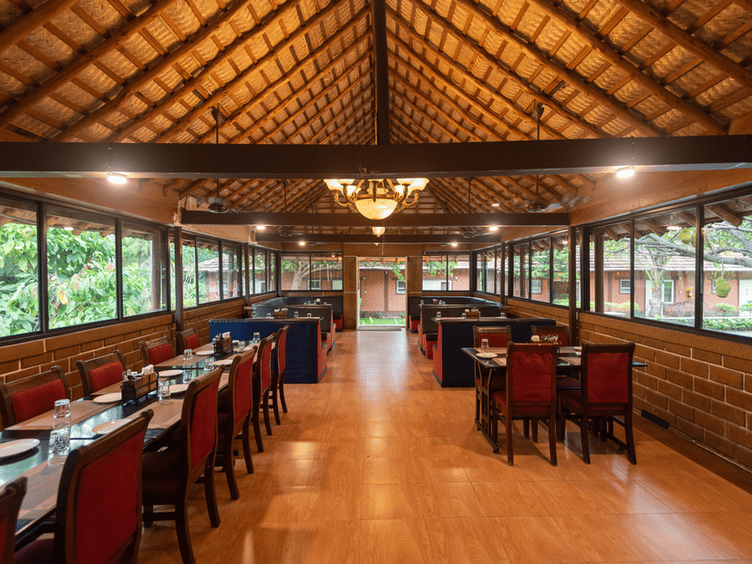 Chairs and tables on either side and a chandelier hanging from the bricked roof in the centre in the Aqua Restaurant at Ibex River Resort, Pollachi.