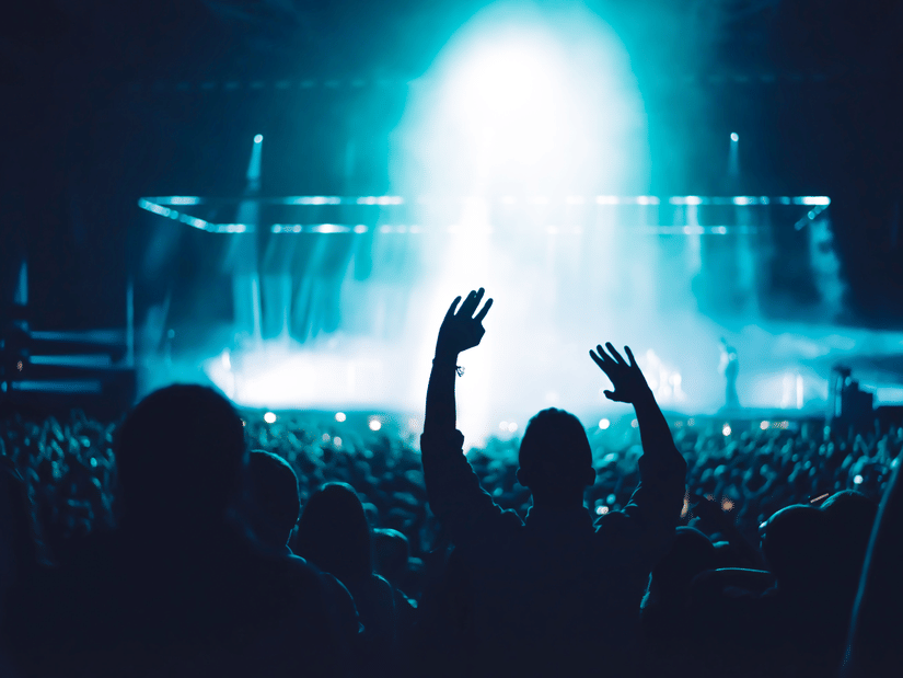 Silhouetted audience watching a live show illuminated by powerful blue stage lights and visual effects