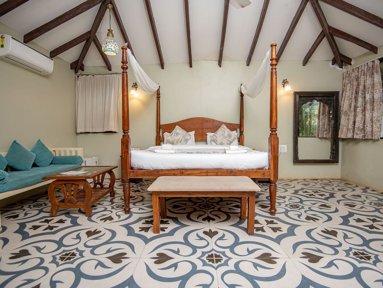 Spacious guest room with two sofas and a canopy bed under a sloped wooden roof at De Soul Santé, Morjim.