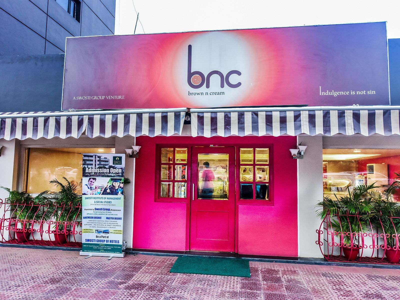 Facade of Brown N Cream with plants on the side of the entrance at Swosti Grand, Bhubaneswar