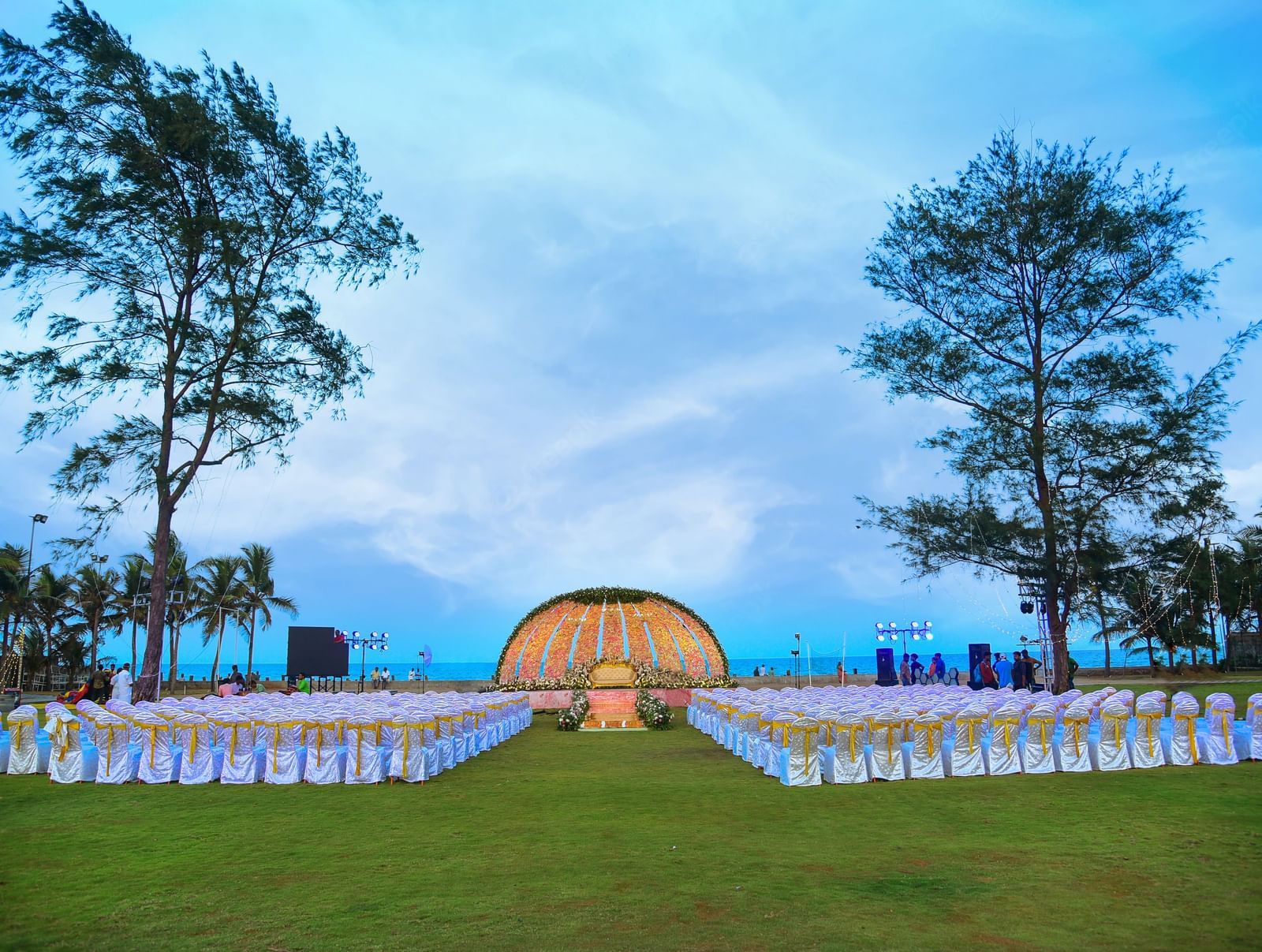 A grand outdoor archway or stage setup on a lawn with a path leading to it, surrounded by white chairs and tables | Grand Bay Resort and Spa