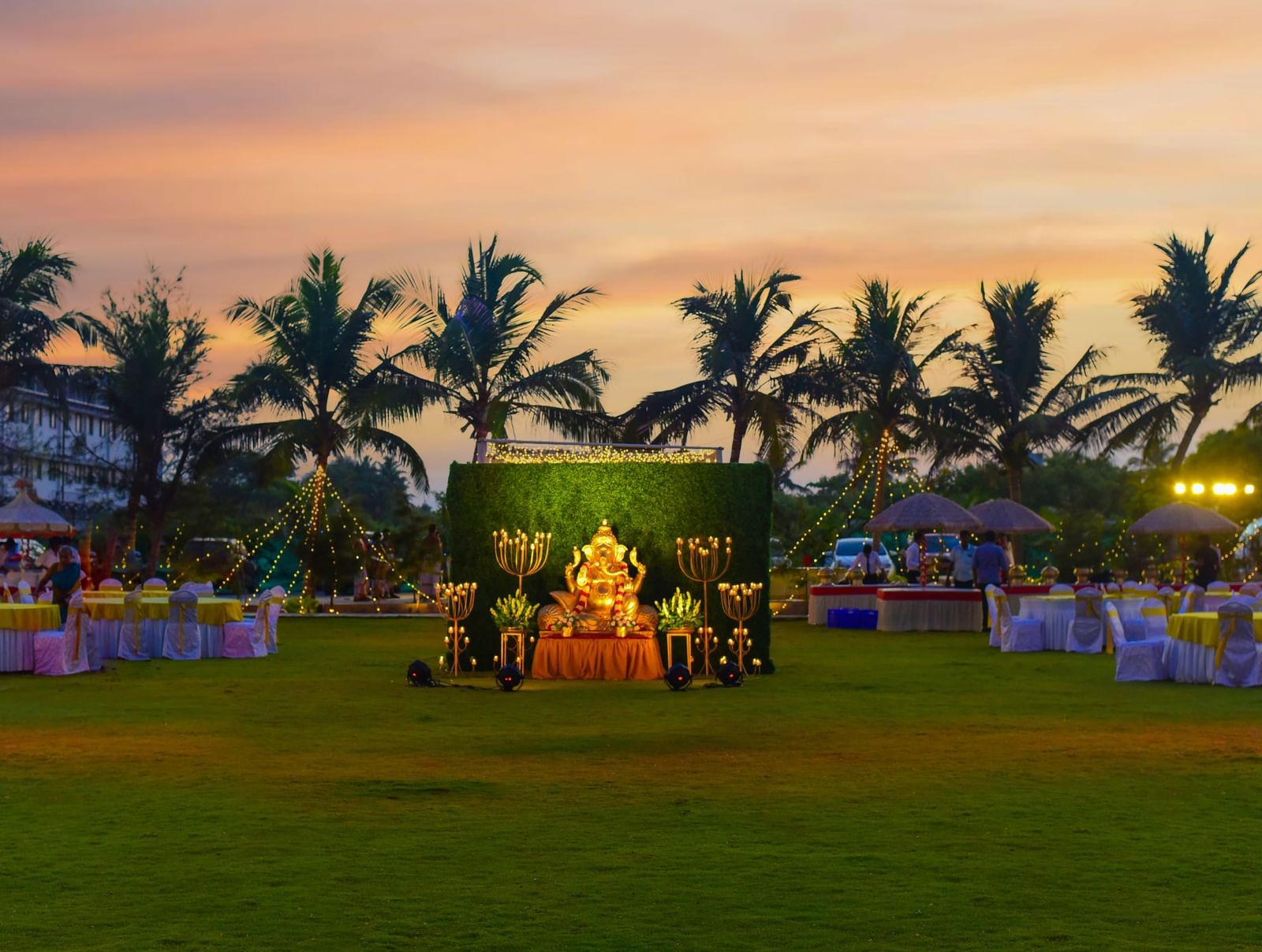 An outdoor evening event setup on a green lawn with a decorated central seating area, surrounded by palm trees against a twilight sky | Horizon | Grand Bay Resort and Spa