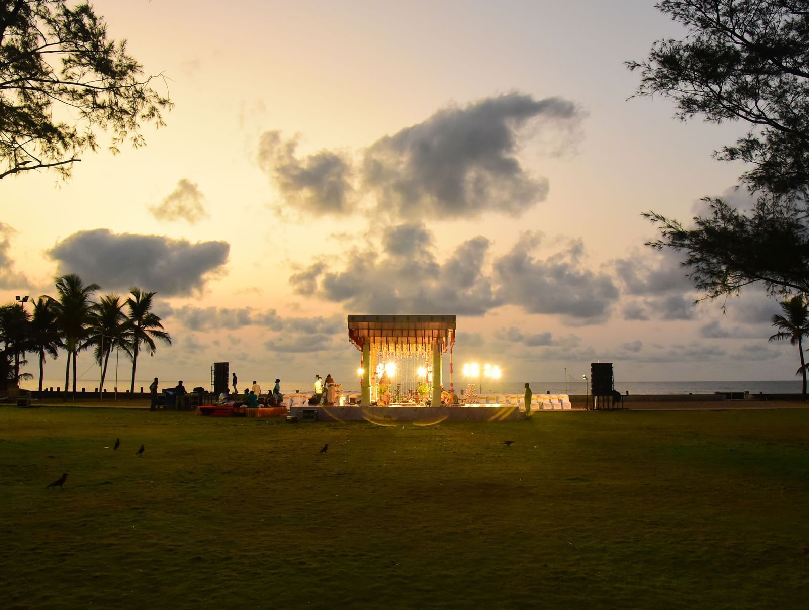 An outdoor event at sunset with a structure resembling a wedding canopy on a beach or grassy area, silhouetted against the colorful sky | Grande Pavillion | Grand Bay Resort and Spa