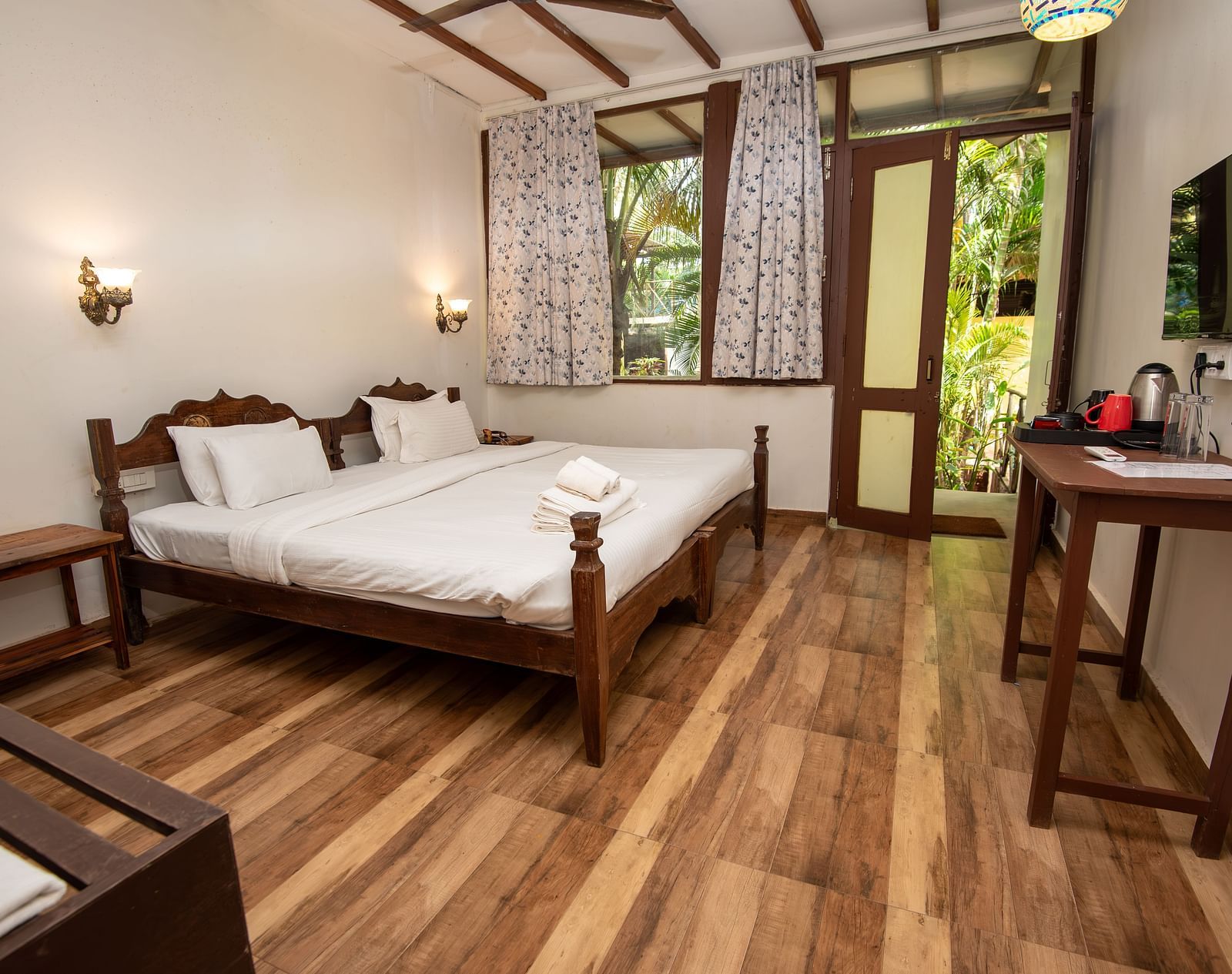 Bright guest room with a double bed, wooden flooring, a flat-screen TV, and natural light streaming in at De Soul Santé, Morjim.